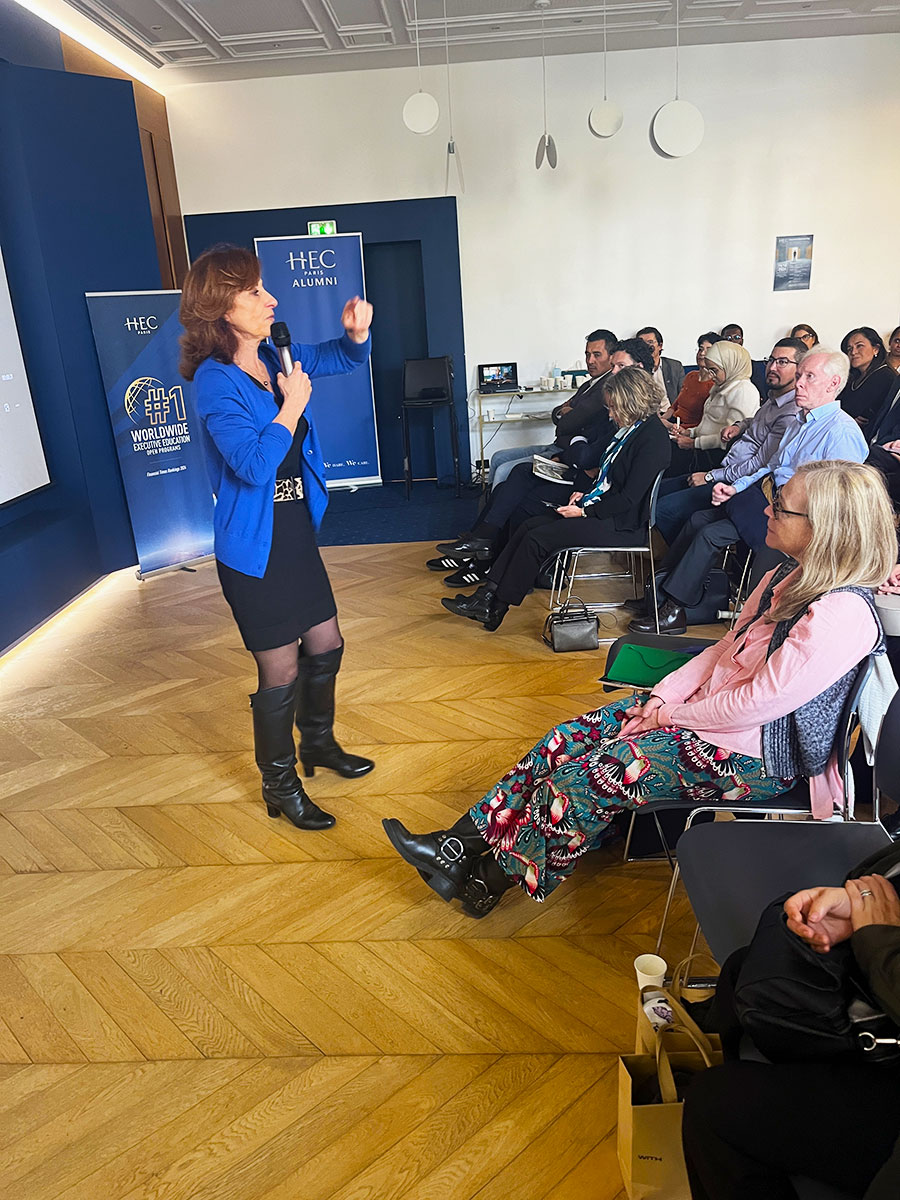 Femme en veste bleue animant une présentation devant un groupe de personnes assises.