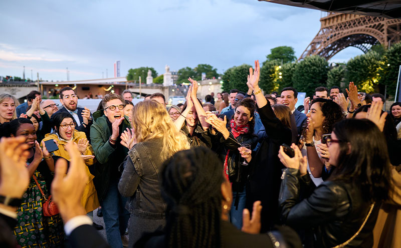 Groupe nombreux de personnes rassemblées sur une place publique, avec la tour Eiffel en arrière-plan.