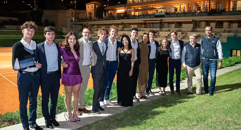 Groupe d'étudiants d'HEC Paris et de partenaires en tenue de soirée posant ensemble devant des courts de tennis lors de l'HEC Clay Court Challenge 2024, dans un cadre nocturne.