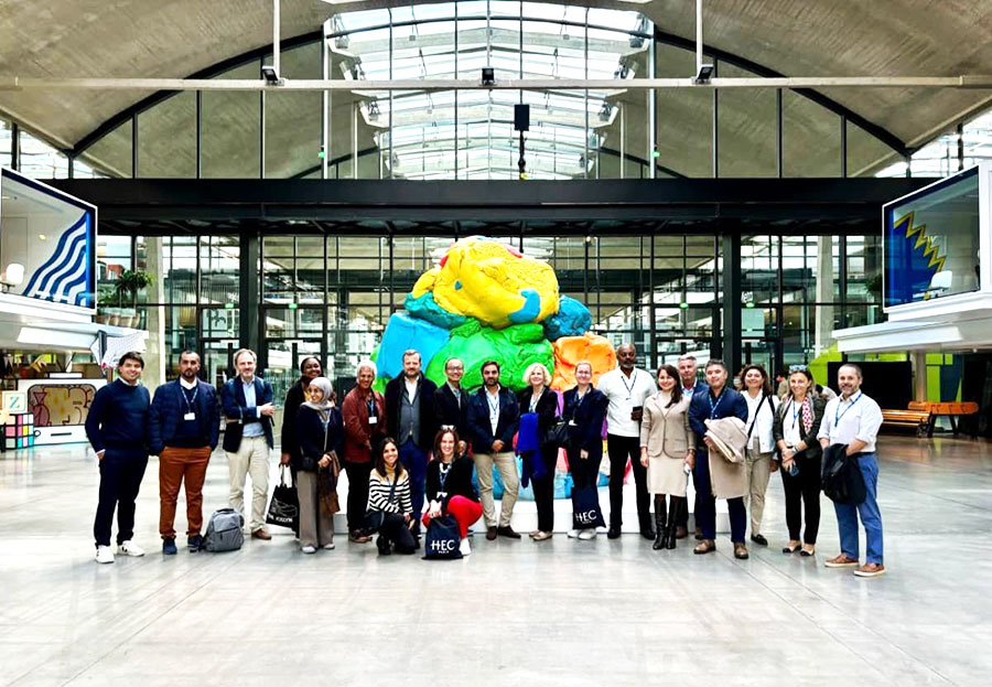 Group of executives and professionals gathered at a modern innovation hub, with a colorful sculpture and industrial-style architecture in the background