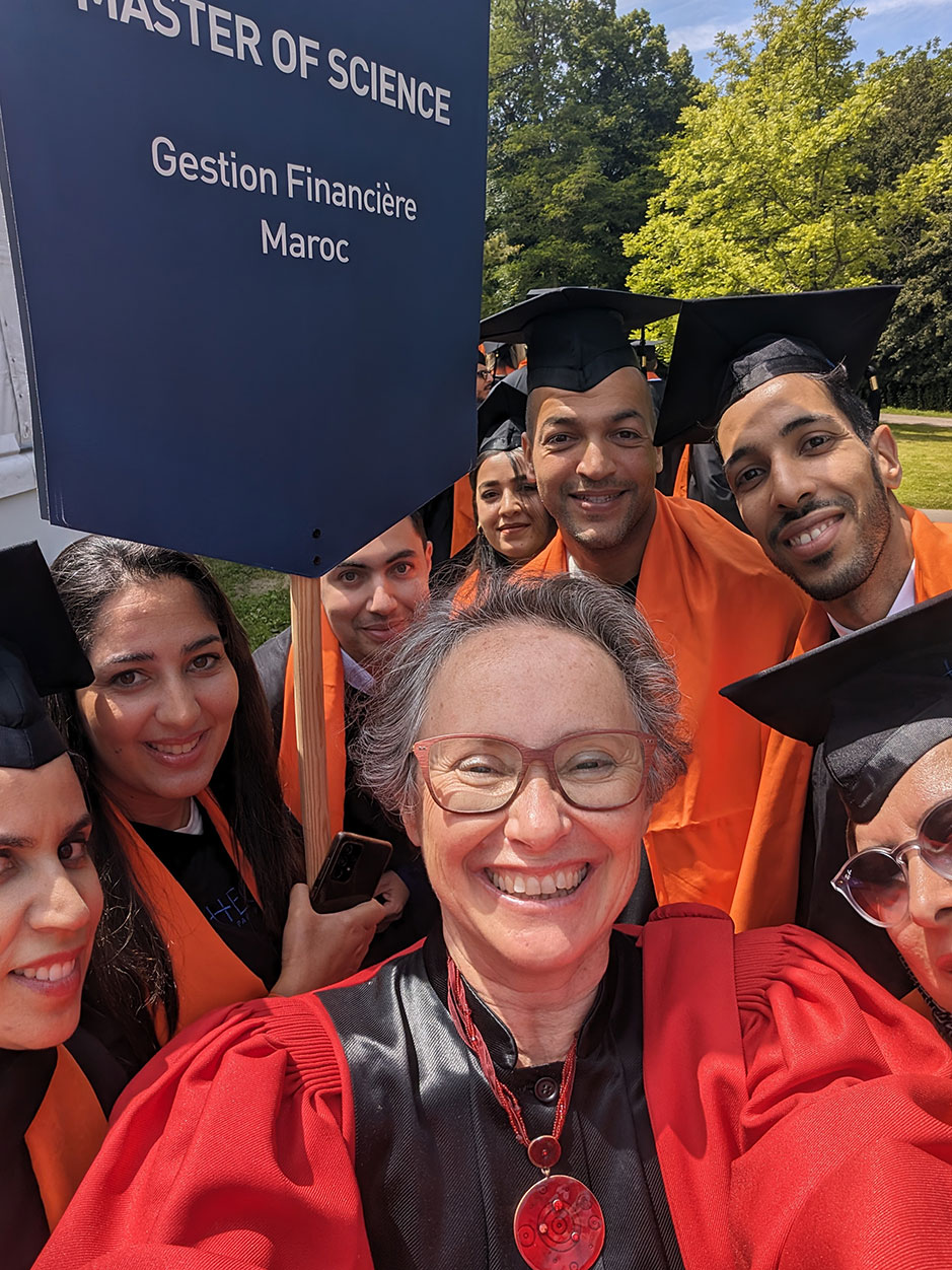 A joyful group of graduates poses for a selfie after a ceremony, holding a sign that reads 