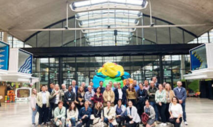 Group of executives and professionals gathered at a modern innovation hub, with a colorful sculpture and industrial-style architecture in the background