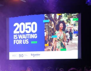 A large indoor event with a stage and an audience seated in a dimly lit room. A screen displays the message '2050 IS WAITING FOR US' along with the logos of HEC Paris, SO, and Schneider Electric