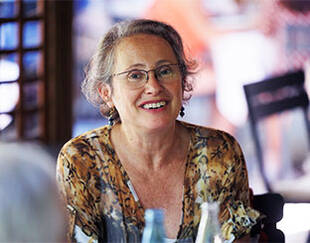 Woman with short, curly hair and glasses, smiling warmly at the camera