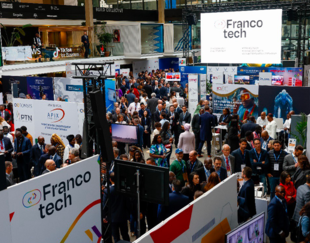 A large crowd attending the FrancoTech event, surrounded by various company booths and technology displays, in a busy exhibition hall