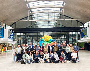 Group of executives and professionals gathered at a modern innovation hub, with a colorful sculpture and industrial-style architecture in the background