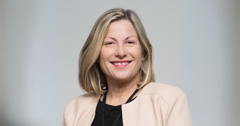 Smiling woman with shoulder-length blonde hair, wearing a light-colored jacket