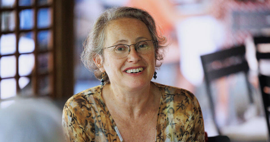 Woman with short, curly hair and glasses, smiling warmly at the camera