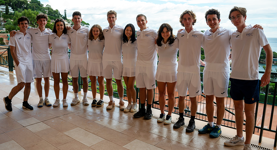 Groupe d'étudiants d'HEC Paris en tenue de tennis blanche posant ensemble lors de l'HEC Clay Court Challenge 2024, avec vue sur la mer et les collines en arrière-plan.